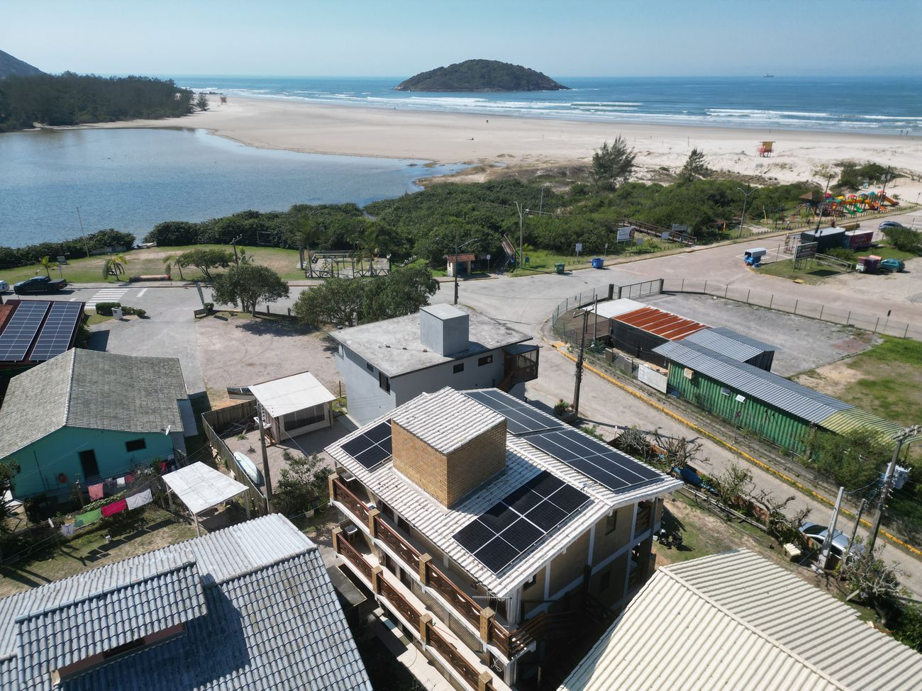 Sistema de energia solar de 12,2 kWp em pousada na Barra de Ibiraquera, Imbituba/SC, com a praia ao fundo