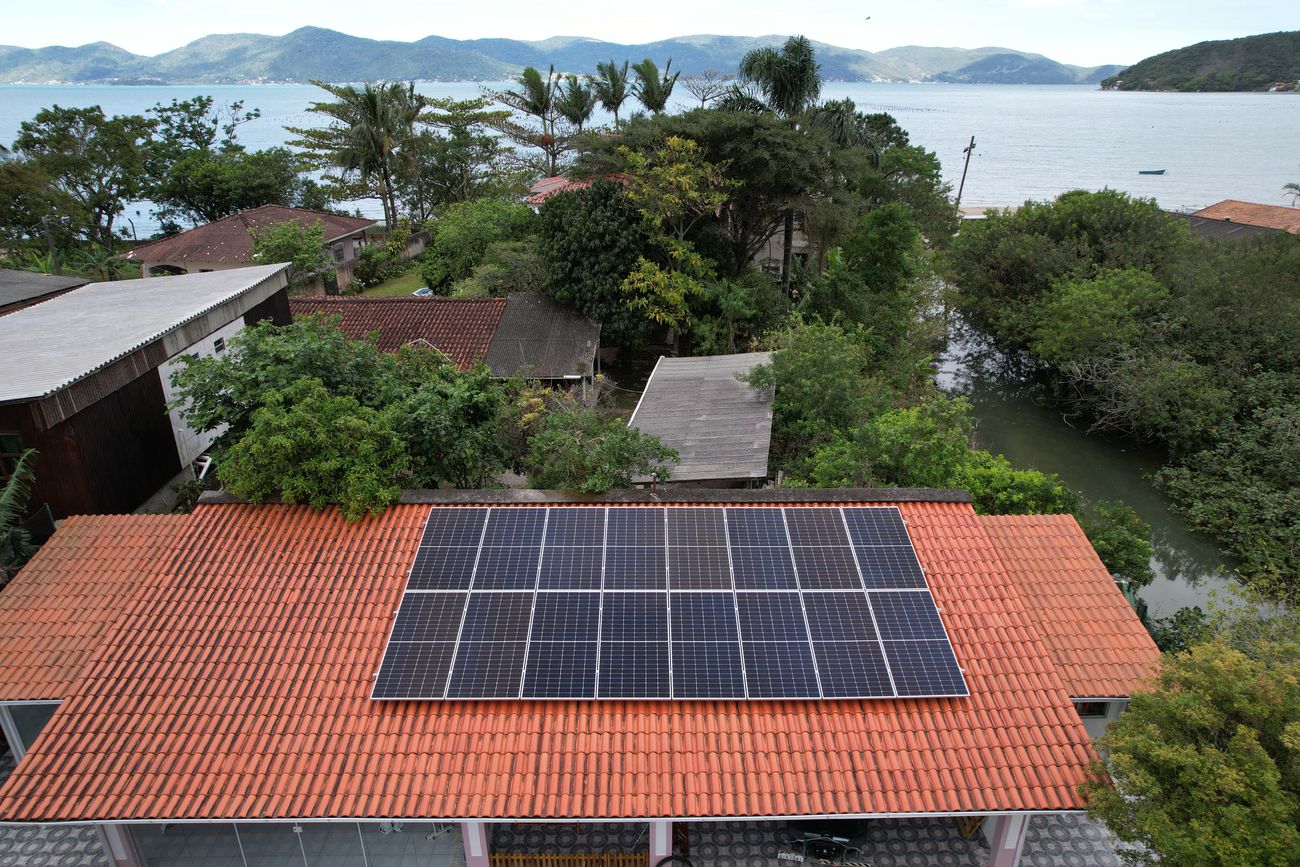 Sistema de energia solar de 9,04 kWp em residência na Enseada de Brito, Palhoça/SC, com a baía ao fundo